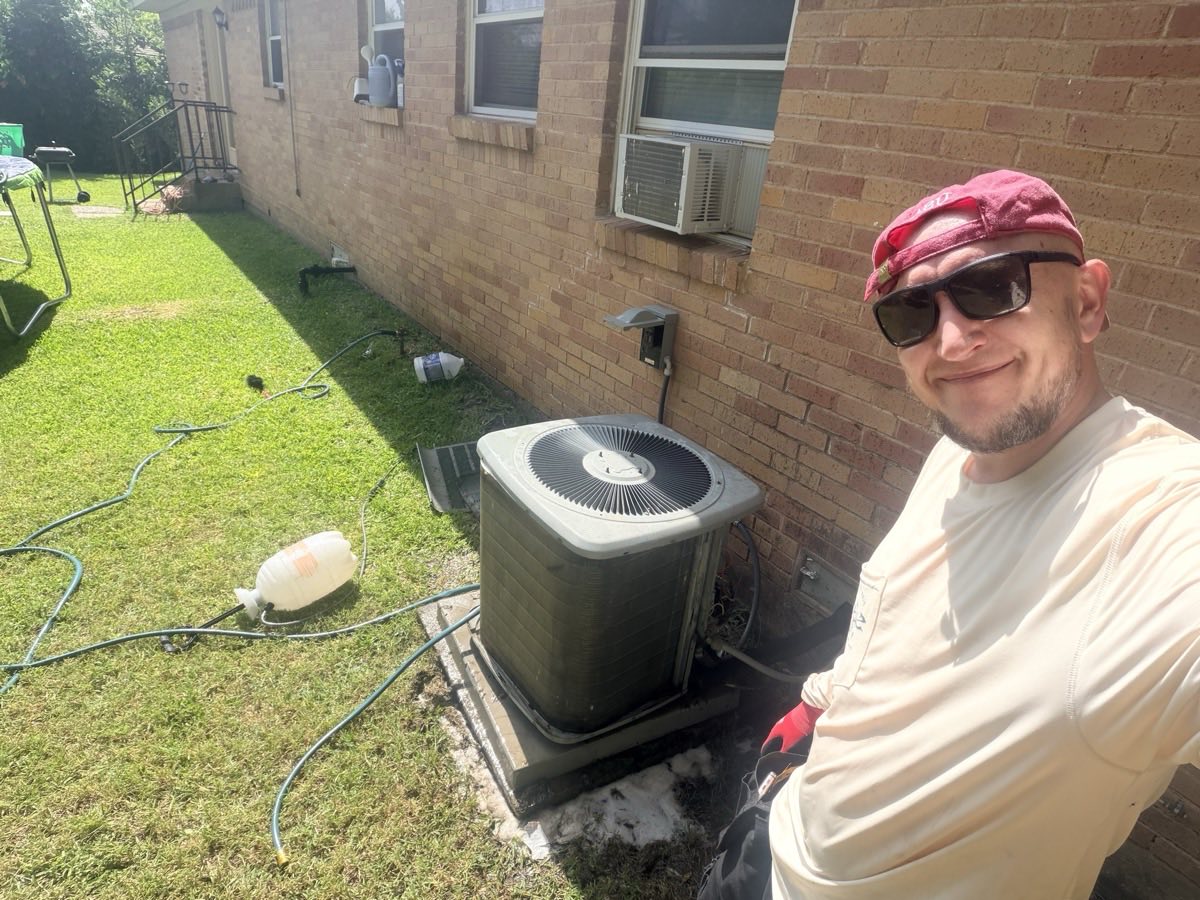 AC/DC technician beside a freshly cleaned residential condenser unit outside a brick home in DFW