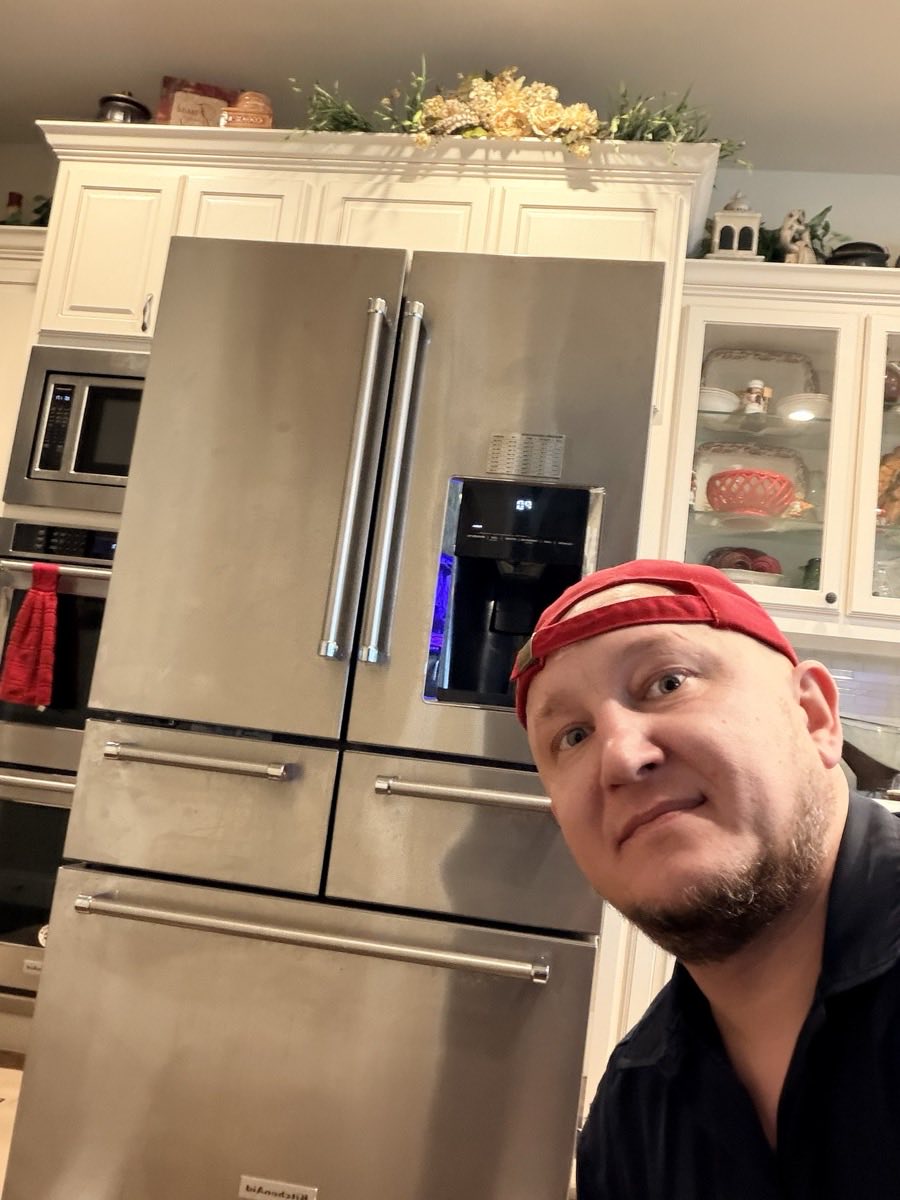 AC/DC technician beside a KitchenAid multi-door refrigerator after a completed service call
