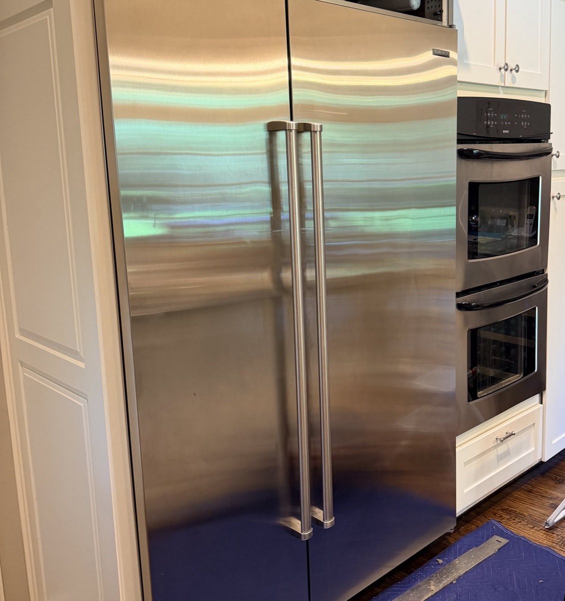 Built-in side-by-side refrigerator and double wall oven back in place in a residential kitchen after a service visit, floor protection still down