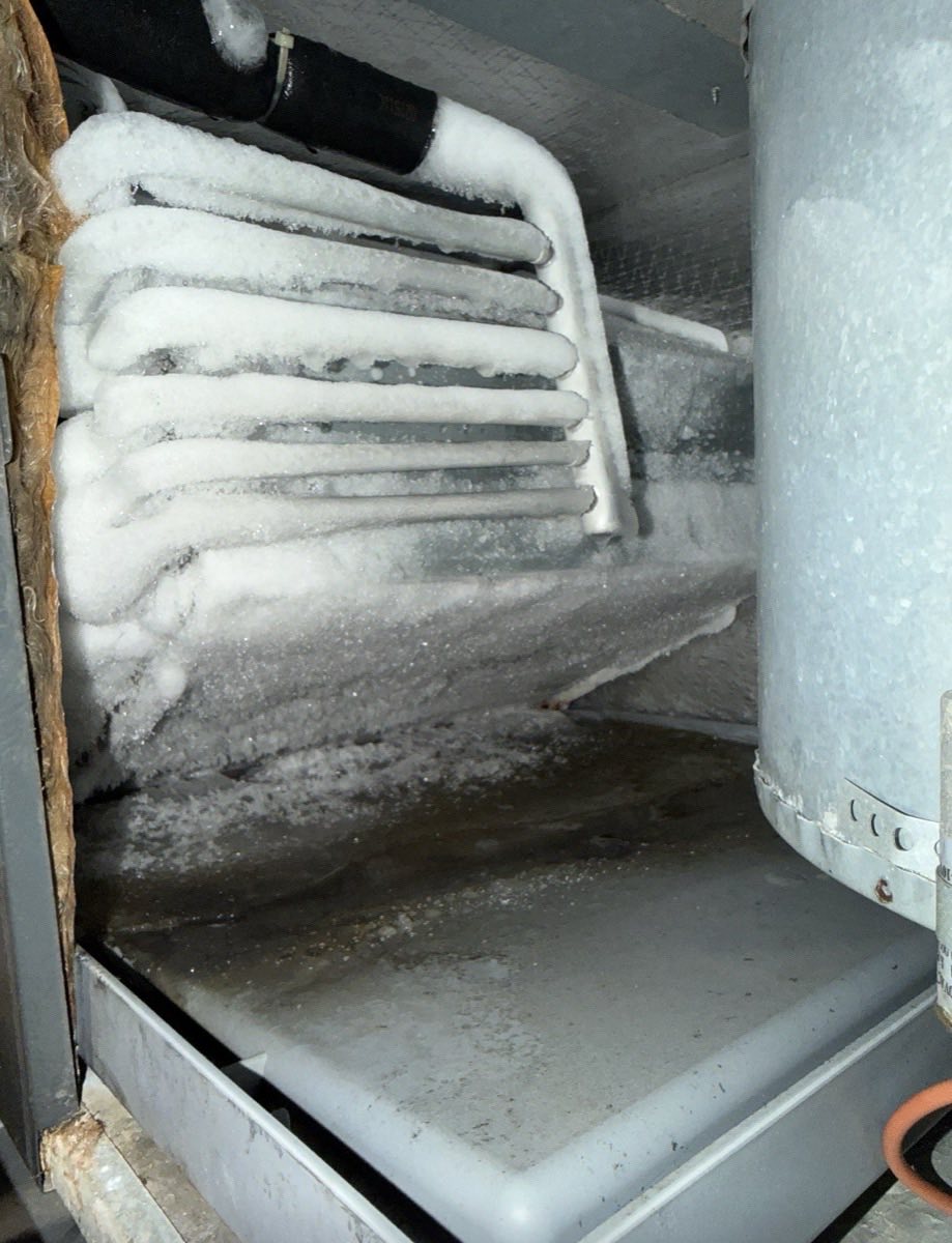 Refrigeration evaporator coil encased in ice with frost across the drain pan below it