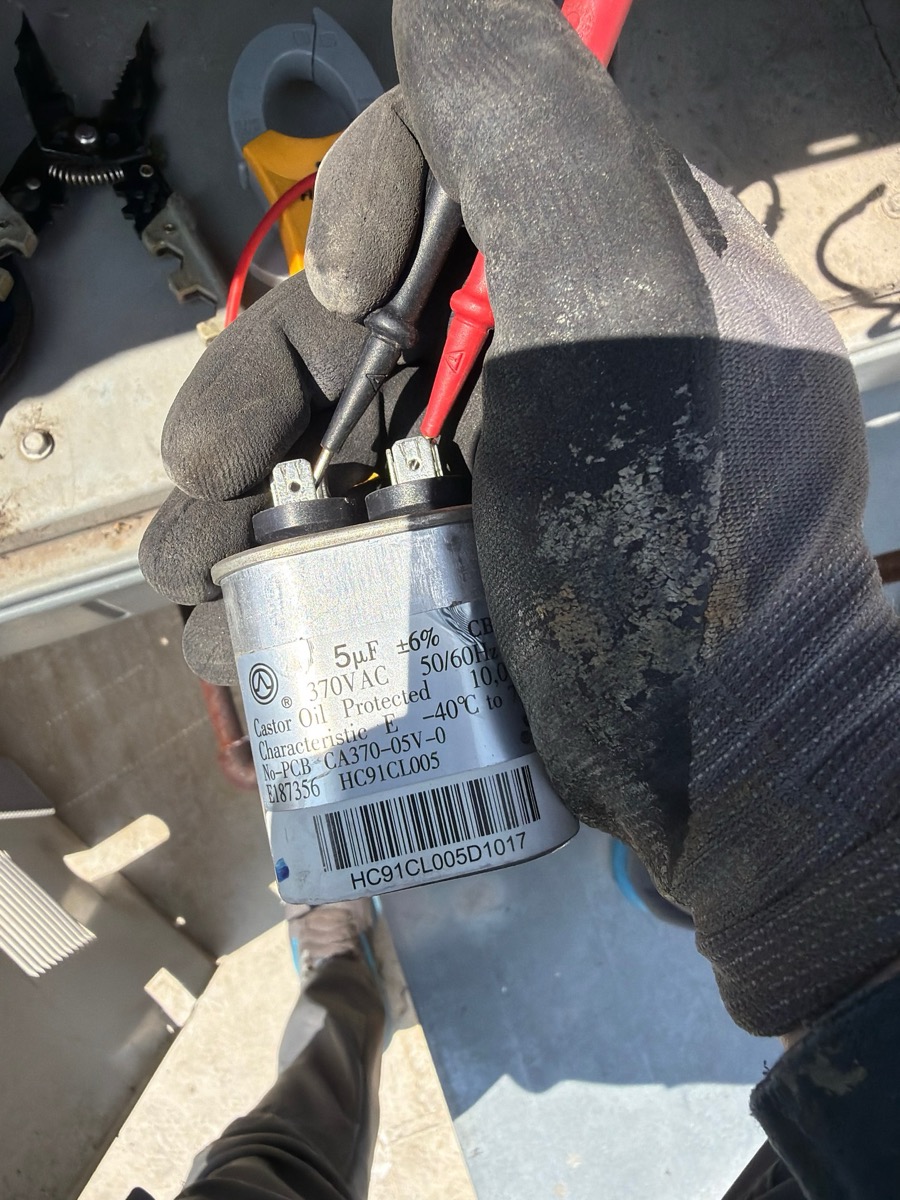Technician measuring a 5 microfarad 370 volt run capacitor with meter leads during an air conditioning diagnostic