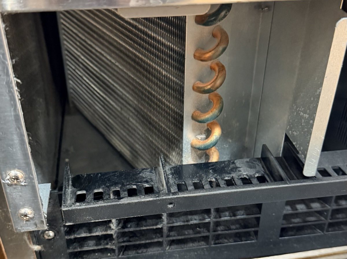Dust-clogged condenser coil inside a commercial ice machine before cleaning