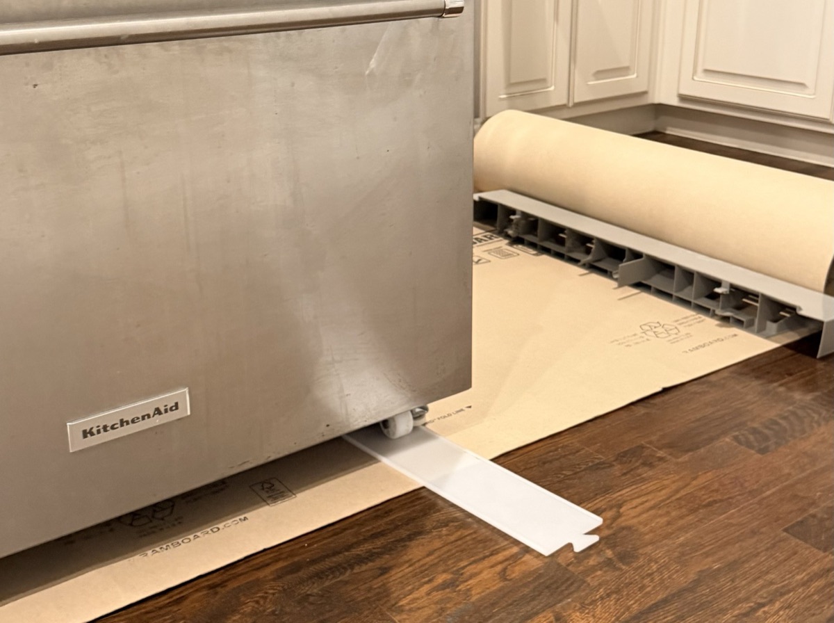 KitchenAid refrigerator on a rolled-out floor runner with a slide board protecting the hardwood floor