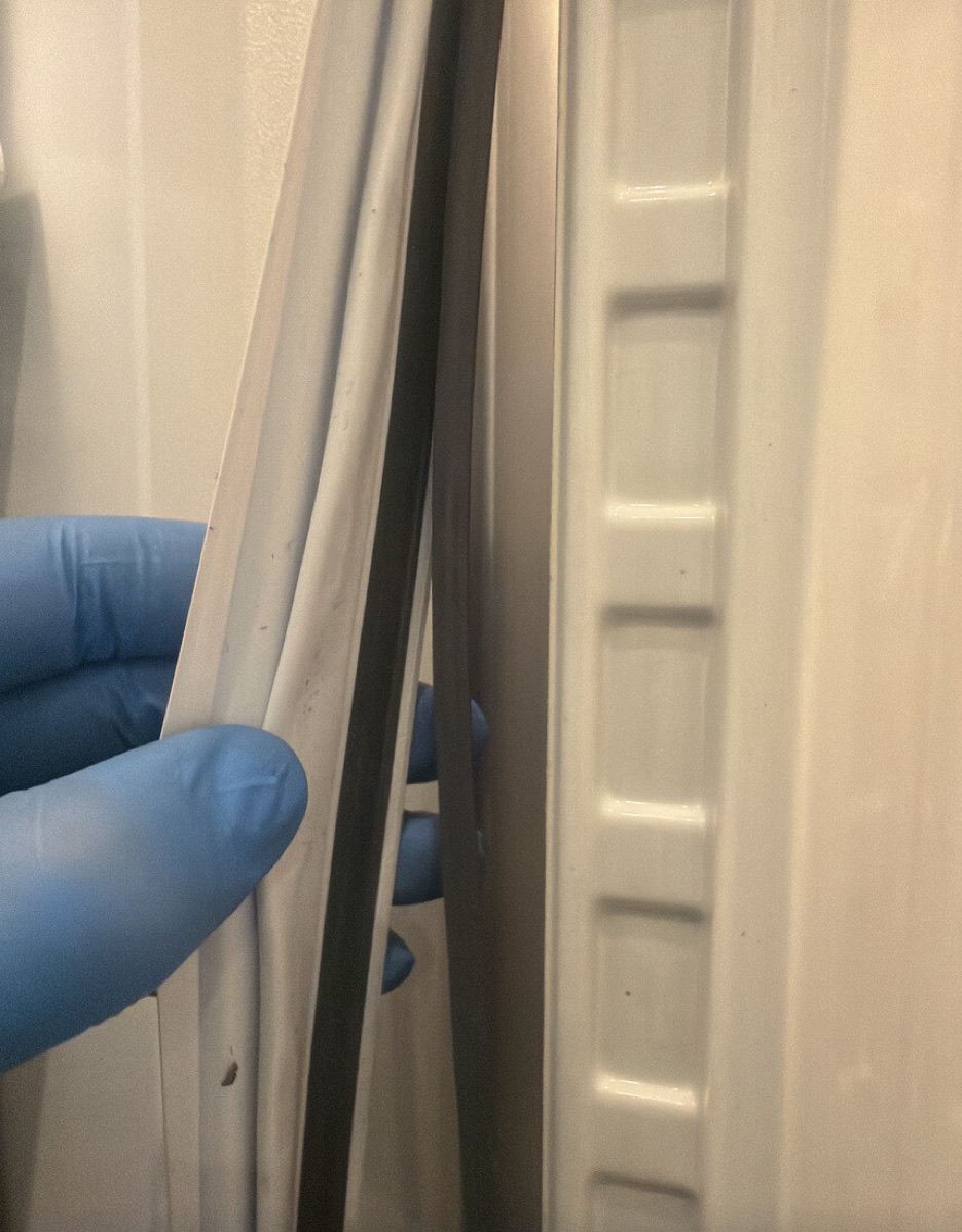 Gloved hand pulling back a refrigerator door gasket to check the seal