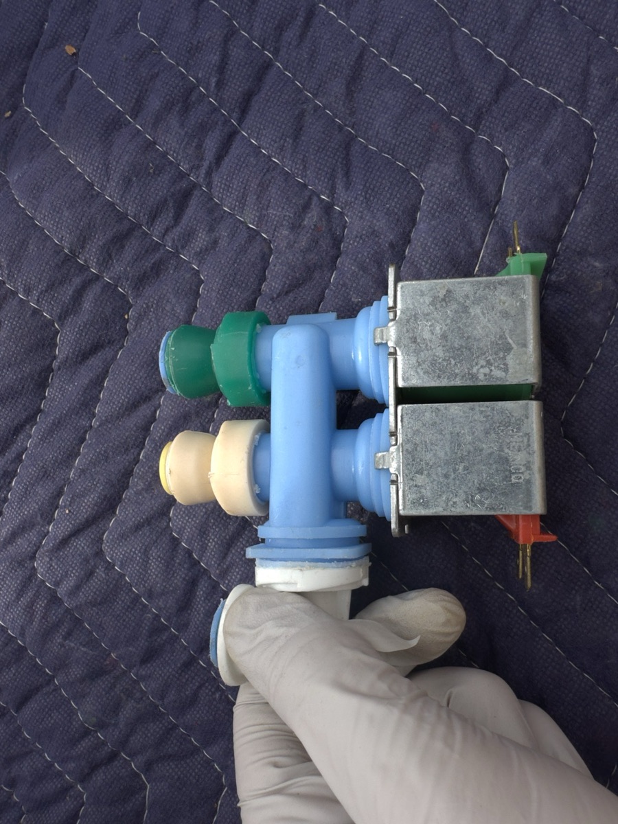 Dual-solenoid refrigerator water inlet valve held in a gloved hand