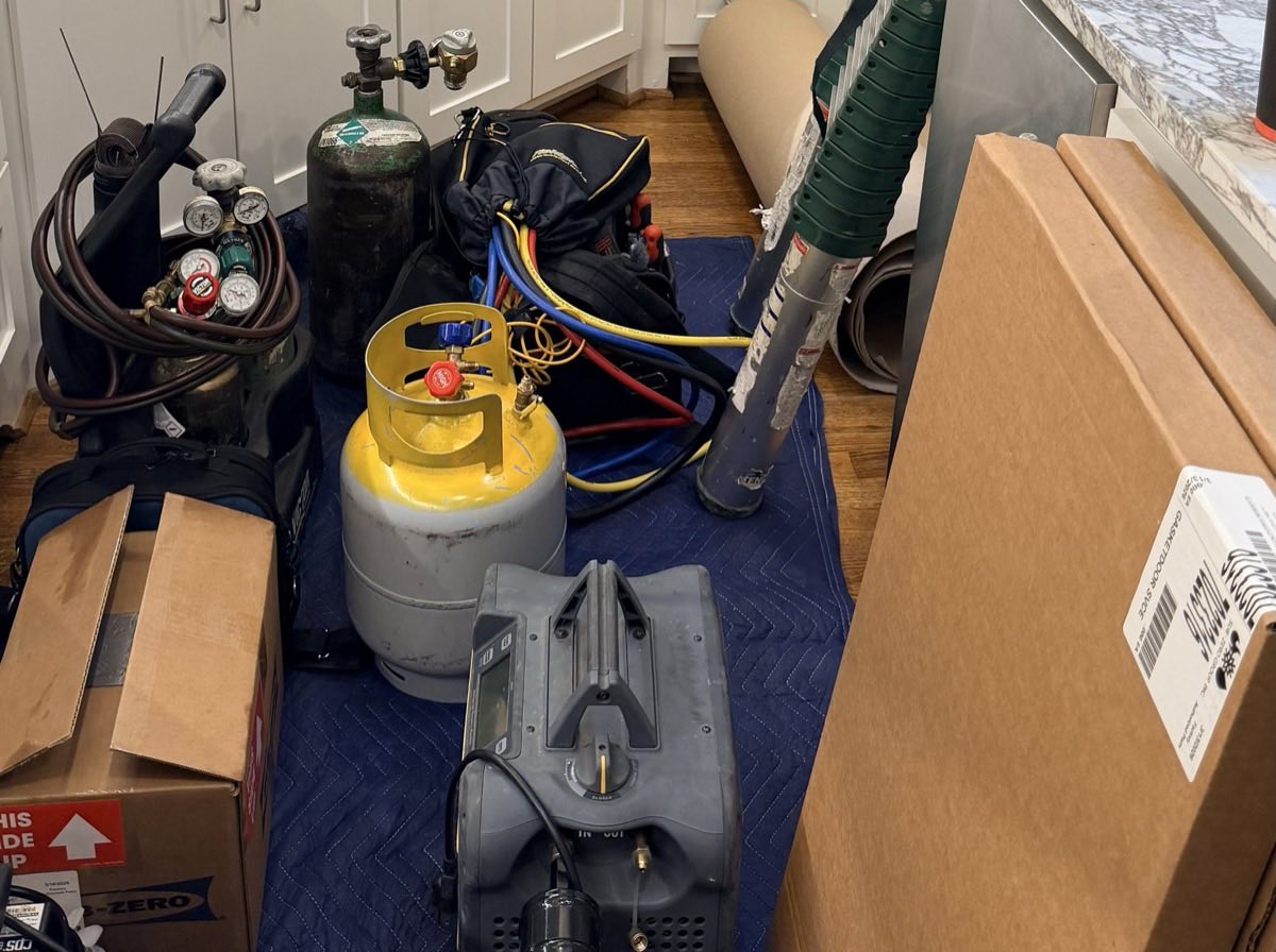 Sealed-system equipment and a Sub-Zero parts box staged on floor protection in a residential kitchen during a repair