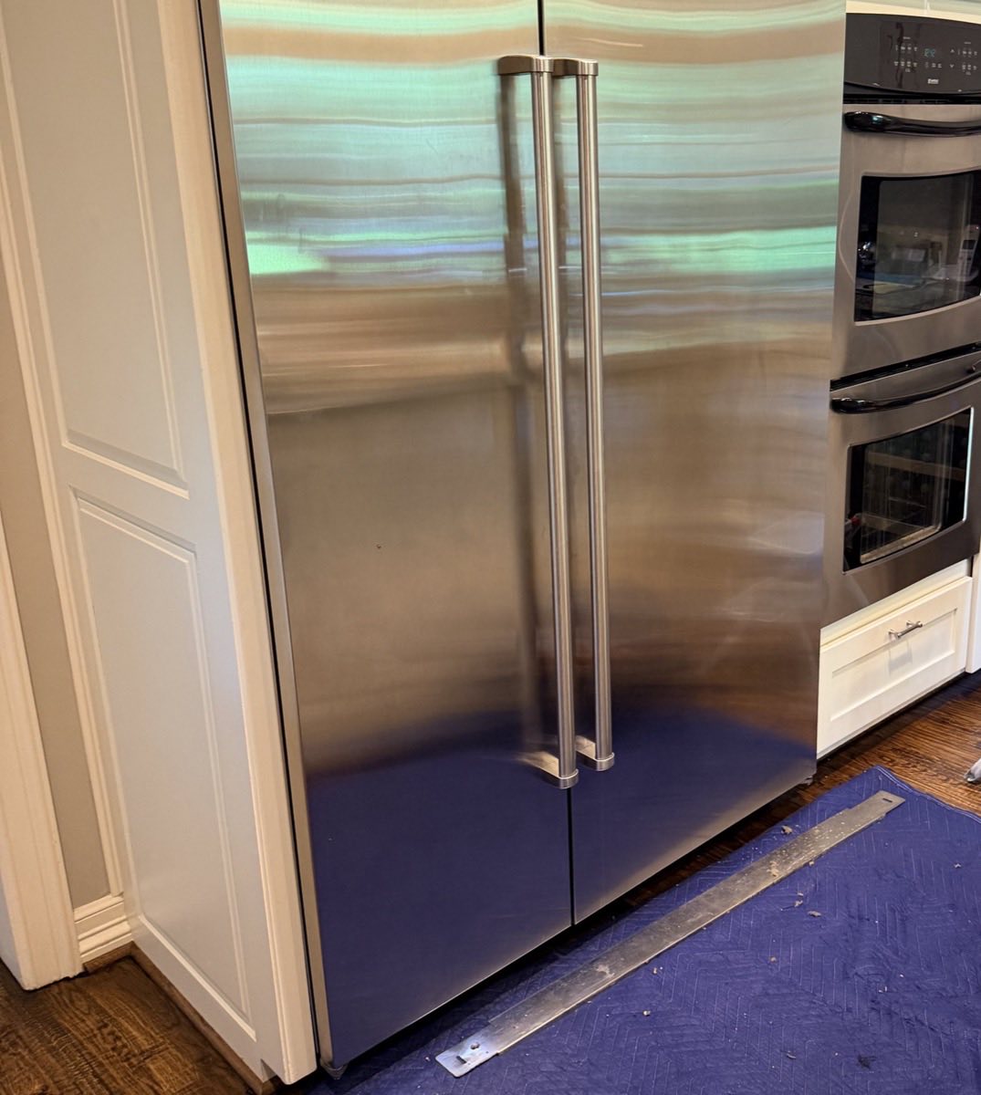 Built-in side-by-side refrigerator back in its cabinet opening after a service call, floor protection still in place