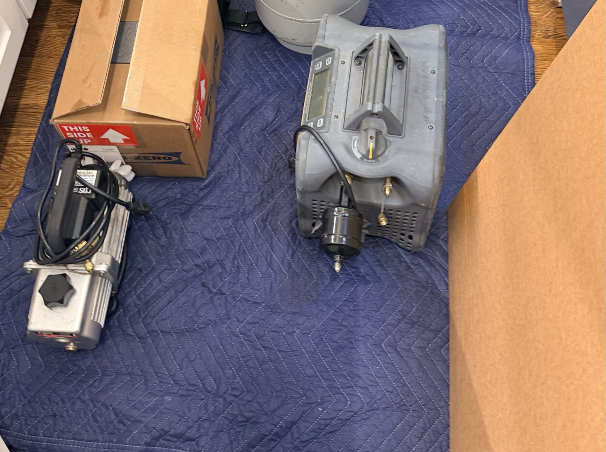 Refrigerant recovery machine and vacuum pump set up on protective blankets beside a Sub-Zero parts carton during a built-in refrigerator repair