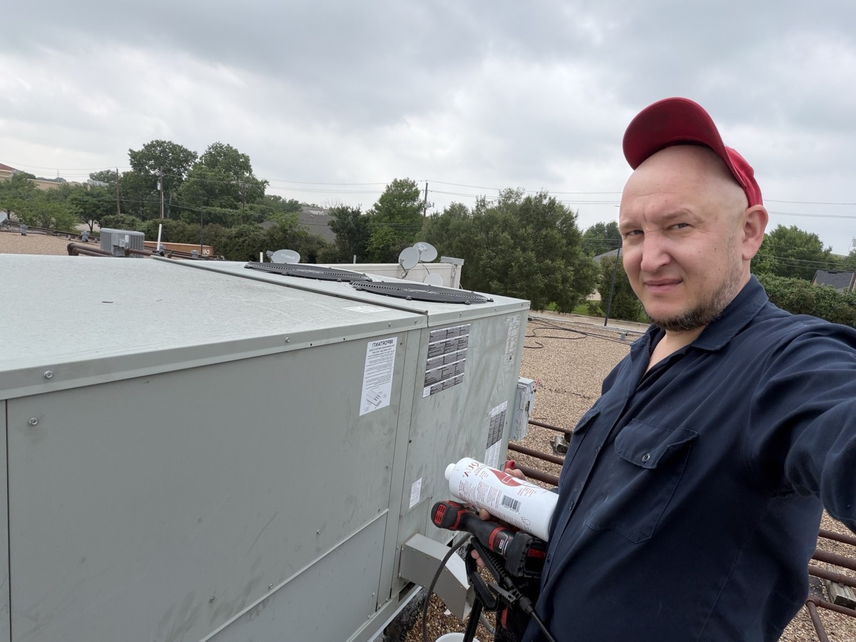 ACDC technician on a commercial rooftop next to a package unit during a maintenance route
