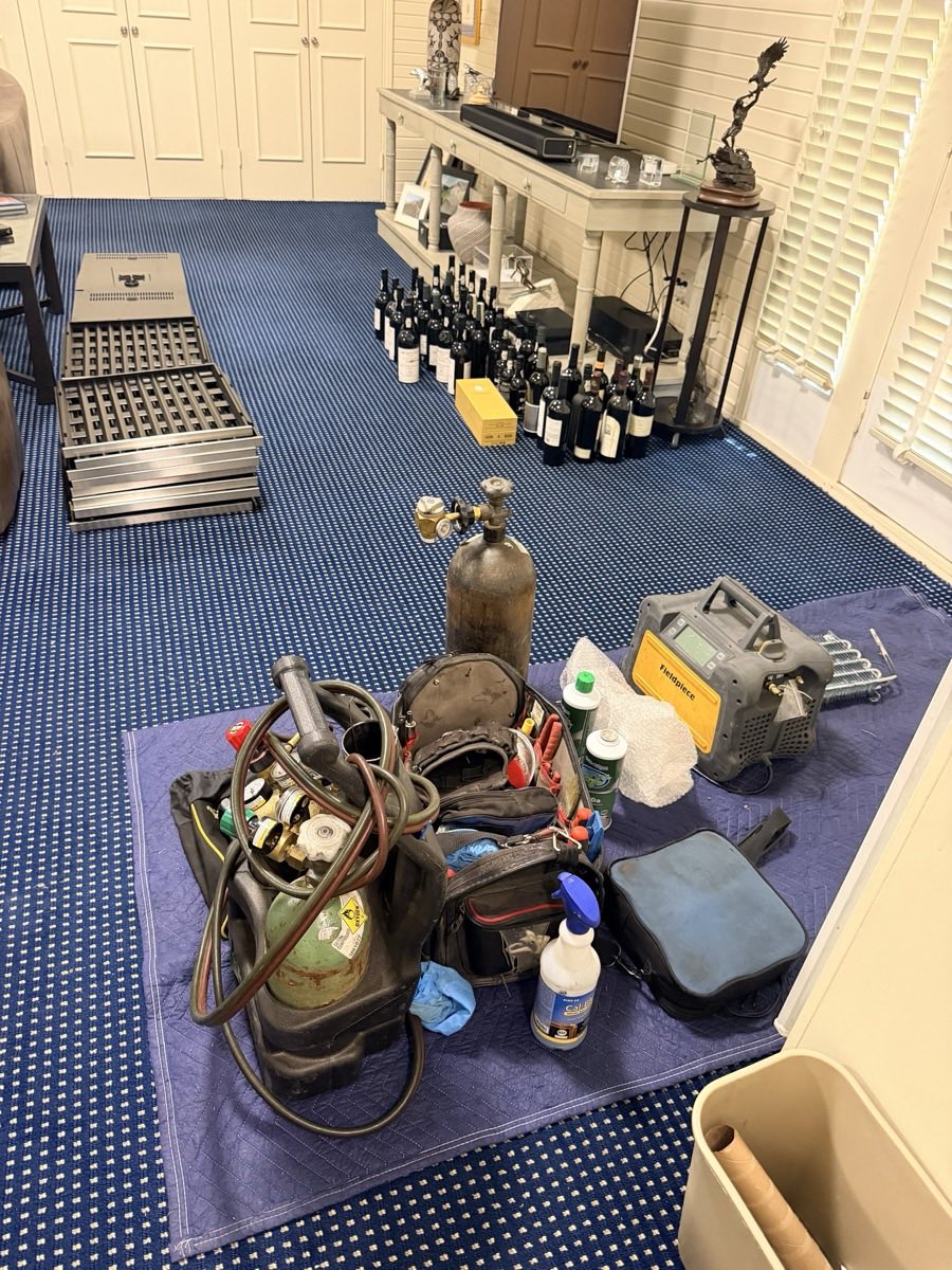 Wine cellar during a sealed-system repair with bottles and racking removed and recovery equipment, gauges and torch set out on floor protection